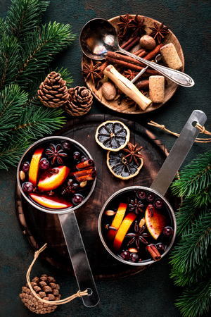 hot mulled wine cooked in two saucepan with spices, orange and cranberries on the table with Christmas fir twigs on a dark backgroundの写真素材