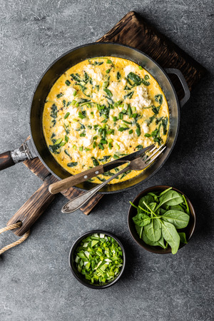 omelette with spinach and cheese in a pan on the concrete background top viewの写真素材
