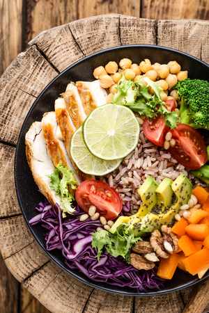 Buddha bowl salad with chicken fillet, brown rice, avocado, pepper, tomato, broccoli, red cabbage, chickpea, fresh lettuce salad, pine nuts and walnuts. healthy food. balanced diet eating. Top viewの写真素材