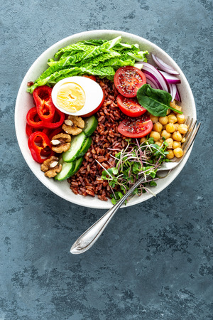 Healthy salad Buddha bowl dish of brown rice, pepper, tomato, cucumber, chickpea, chia, sprouts, savoy and nuts. Healthy eating trend, superfood. Top viewの写真素材