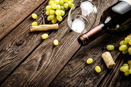 wine background of open wine bottle, wine glass and branches of white grapes on a dark wooden rustic background with blank space for a textの写真素材