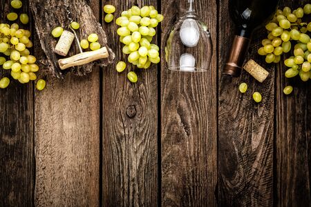 wine background of open wine bottle, wine glass and branches of white grapes on a dark wooden rustic background with blank space for a textの写真素材