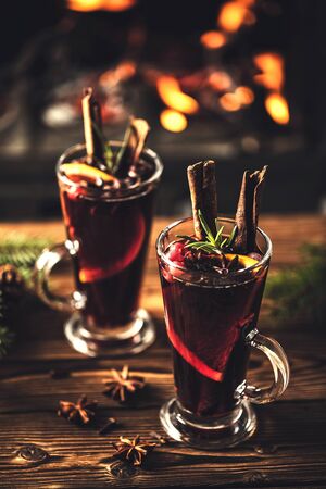Mulled wine with spices in glasses on a wooden table against the background of a fireplace fire. Winter drink traditional for the Christmas holidays.の写真素材