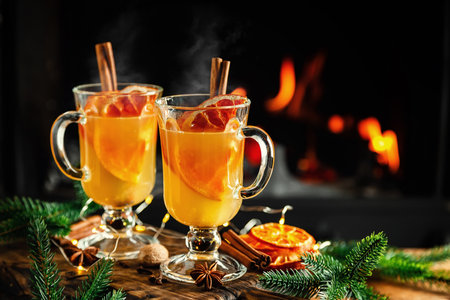 Mulled cider glasses on the background of fireplace fire. Hot mulled spiced apple cider cocktail for winter or autumn time.の写真素材