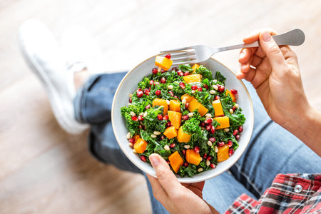 Vegetable salad bowl in woman hands. Fresh kale and baked pumpkin salad. Healthy eating conceptの写真素材