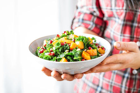 Vegetable salad bowl in woman hands. Fresh kale and baked pumpkin salad. Healthy eating conceptの写真素材