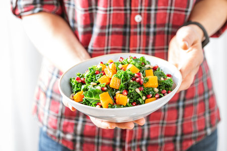 Vegetable salad bowl in woman hands. Fresh kale and baked pumpkin salad. Healthy eating conceptの写真素材