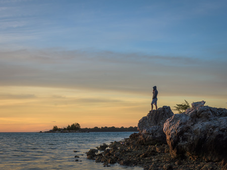 A man stands on a rock with a colorful dawn sky at Harapan Islandの写真素材