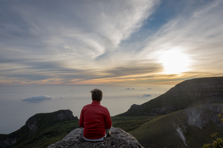 A man sitting and enjoying sunrise on the rock at the top of Gede Pangrango Mountainの写真素材
