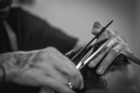 Professional hairdresser performing modern male haircut with scissors in hairdressing salonの写真素材