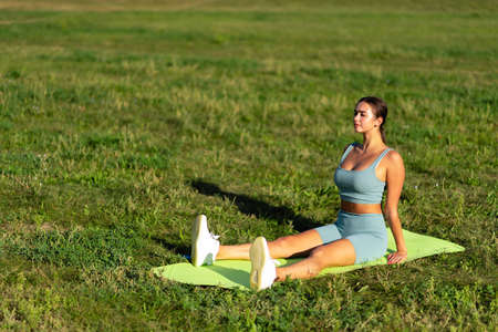 A beautiful sportive girl is engaged in yoga on green grass in a city park. Prapadasana pose