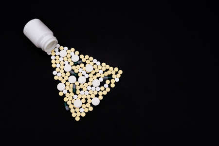 Capsules and tablets of white and yellow color poured out of the jar. Black background