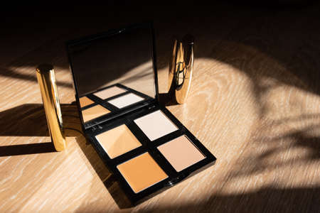 A set of decorative cosmetics. Eyeshadow and lipstick in golden packaging on wooden backgroundの写真素材