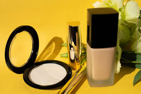 Decorative cosmetics. Powder, foundation and lipstick on a yellow background. Decoration flowers