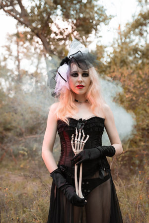 Halloween. A witch in a black suit with red lips stands with a skeleton hand in the smoke. Verticalの写真素材