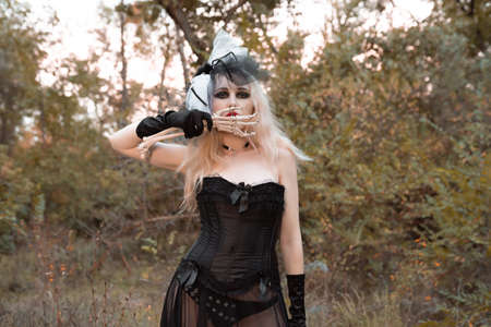 Halloween. A witch in a black suit with red lips holds a skeleton hand near the faceの写真素材