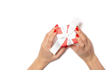 Beautiful hands with red varnish hold a gift on a rich white background. Perfect manicure. Concept for New Year, Christmas, Valentine's Day, giftsの写真素材