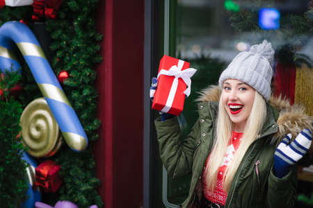 Smiling, happy and excited blonde girl in a warm hat, holding a gift box, smiling and looking at the camera. Christmas conceptの写真素材