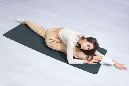 Gorgeous slim girl in a tracksuit doing stretching on a fitness mat. View from above. Stretching and...