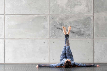 Beautiful sports fitness girl with pigtails. Doing yoga. Lies with legs raised up against the...