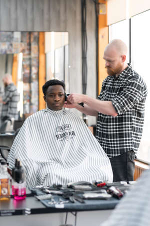 A young African visits a barbershop. Tidying up the beard with the help of a hairdresser. Personal care, male beautyの写真素材