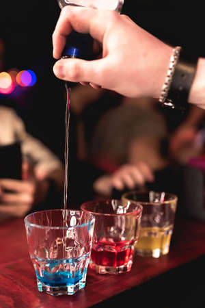 The bartender prepares colorful cocktails in the bar. Bartender's hand close up