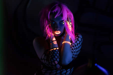 Beautiful girl with fluorescent makeup, unusual colorful prints glow in ultraviolet light in a dark room. Night club, party concept. Russia, Rostov-on-Don 13oct2019のeditorial素材