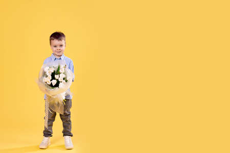 The little boy flowers. Happy smiling child holding a bouquet. Fashion stylish baby with tulipsの写真素材