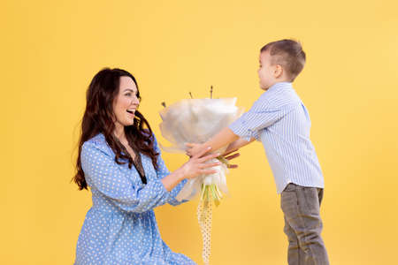 A little son congratulates his mother, gives flowers. A sincere mother hugs her little son of preschool age. March 8, congratulations on International Women's Day, flowers in handsの写真素材