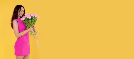 Beautiful girl with a bouquet of pink tulips. Smiling young woman with flowers on a yellow background. Bannerの写真素材