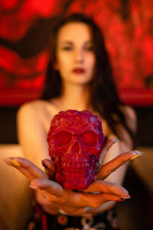 Beautiful girl in a corset holds a figure of a skull in her hands. Focus on the skull. Halloween...