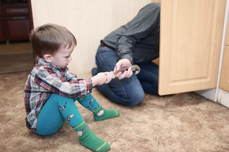 boy helping his father repair the plumbing in the kitchenの写真素材