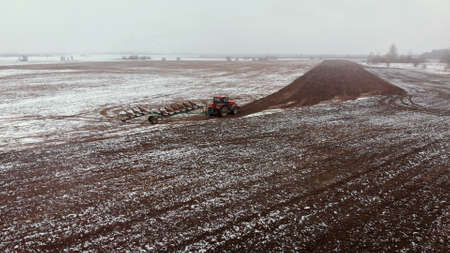 Tractor untimely processes farmland in the spring in a snowfall. Risky farming in adverse weather...