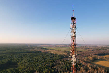 Telecommunication tower on the background of blue sky in a wooded area held by fastening cables. Antenna of the structure transmits signals from cellular mobile phones.の写真素材