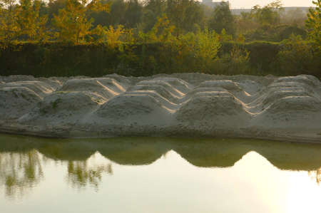 The water of the lake brings a balance of contrasts. A reflection of the dunes on the calm surface of the lake. The arrangement of sand dunes points to order. Dead sand and rich vegetation. Sand dunes on the shore of the fishpond.の写真素材