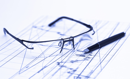 Glasses on stock chart in blue lightingの写真素材