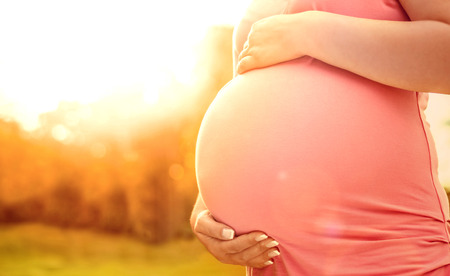 Pregnant woman relaxing in nature on a beautiful sunny day and holding her pregnant stomach with her handsの写真素材