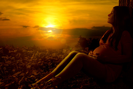 Pregnant woman holding belly against sunset sunlight.の写真素材