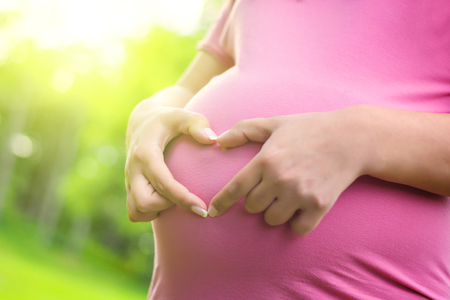 A crop of a pregnant woman's stomach with field in the background.の写真素材