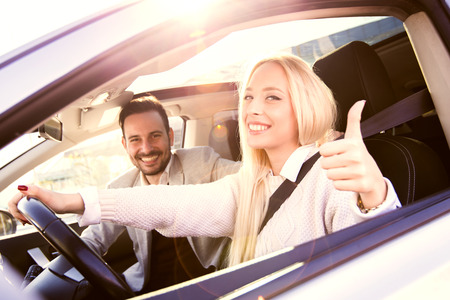 Young man and woman smile at the camera while seated in a new convertible car.