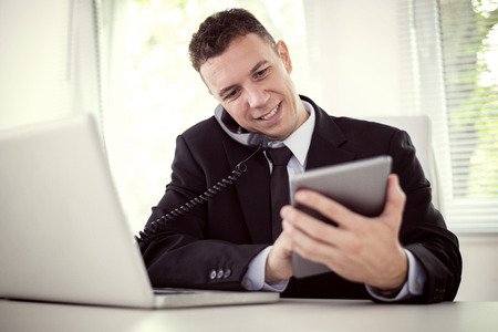 Businessman working on his laptop in the office.Businessman talking on the phone .He is wearing a black suit and a black tie.の写真素材