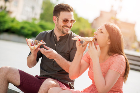 Portrait of an happy couple.They are laughing and eating pizza and having a great time.の写真素材