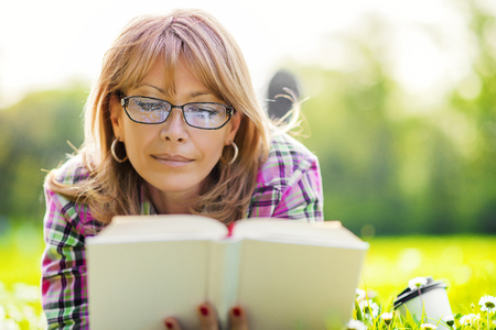 Woman reading outdoors.Happy woman reading a book during springtime in nature.の写真素材