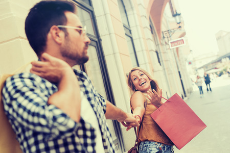Bored man shopping with his girlfriend in the city.Beautiful young loving couple carrying shopping bags on shoulders.の写真素材