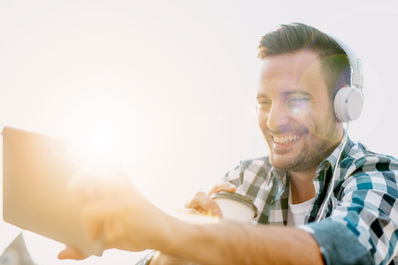 Close up of a young man sitting outdoors listening to music.He is enjoying the music.の写真素材