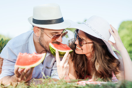 Happy couple on a picnic eating watermelon and smiling at each other on a sunny day.の写真素材