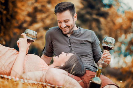 Cute young couple drinking wine on a picnic, smiling at each other on a sunny day.の写真素材