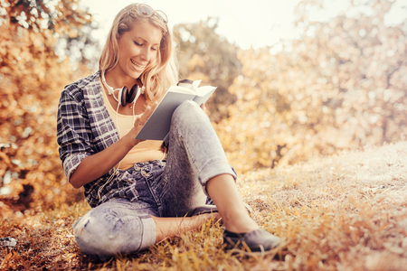 Portrait of a gorgeous young woman reading a book in the autumn park.の写真素材