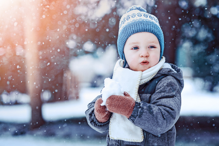 Portrait of toddler boy in winter clothes with falling snow