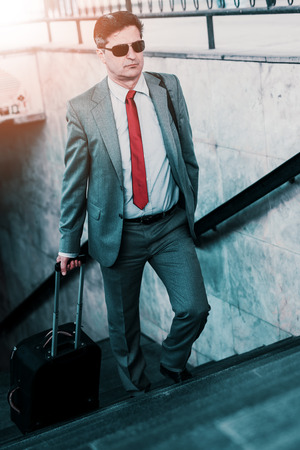 Elegant businessman walking with suitcase outside airport.の写真素材